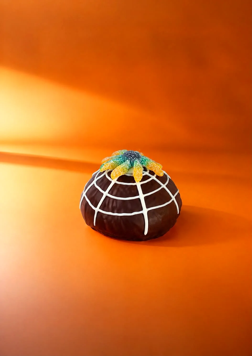 Bomba cubierta de chocolate con telaraña de chocolate blanco y una araña de gominola encima